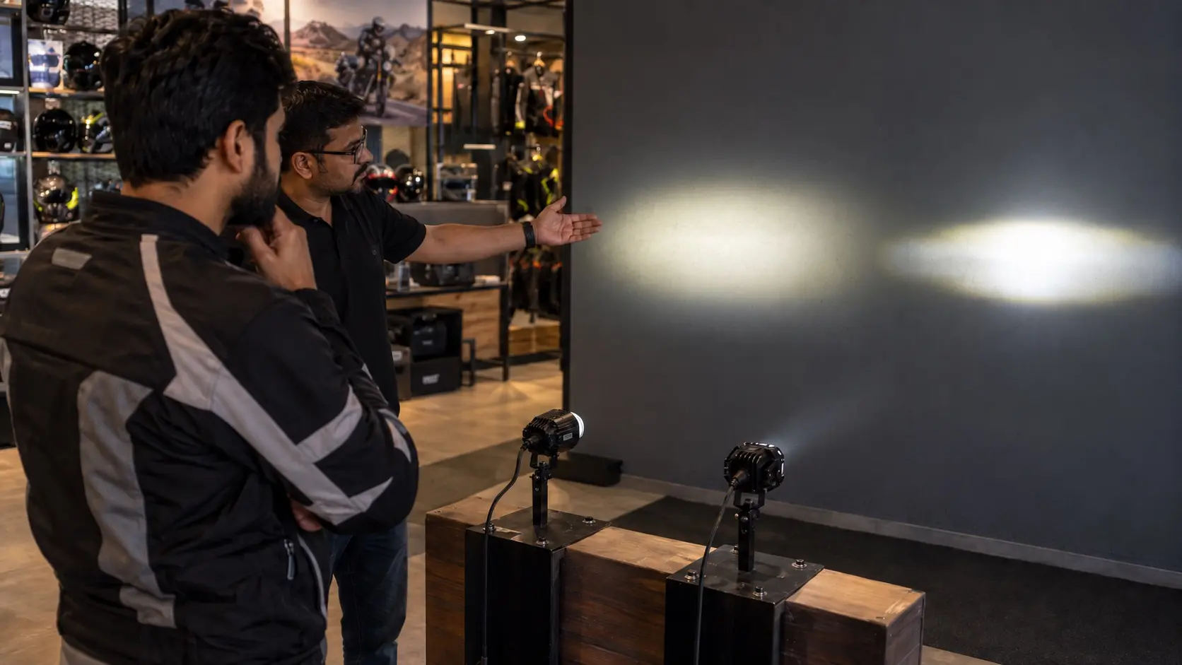 An Indian rider comparing two auxiliary motorcycle lighting options with a specialist in a professional accessories store.