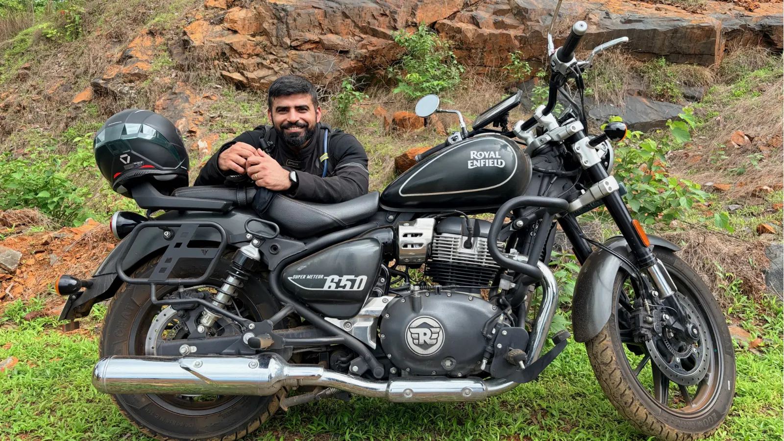 Rider relaxing beside a Royal Enfield Super Meteor 650 during a break on a group ride.