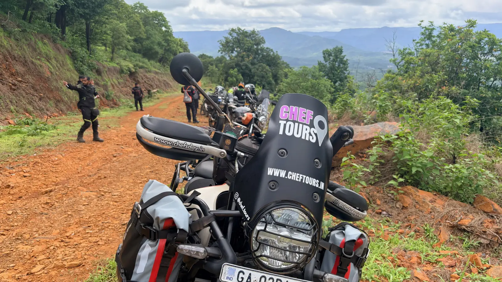 Alan D Mello's adventure motorcycle parked beside a forest trail while fellow riders pause to take in the scenery along the route.