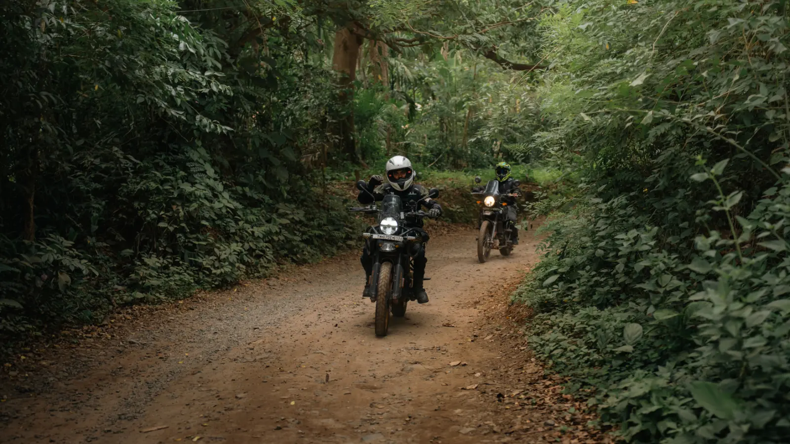 Adventure riders making their way along a narrow forest trail beneath a dense canopy in the Western Ghats.