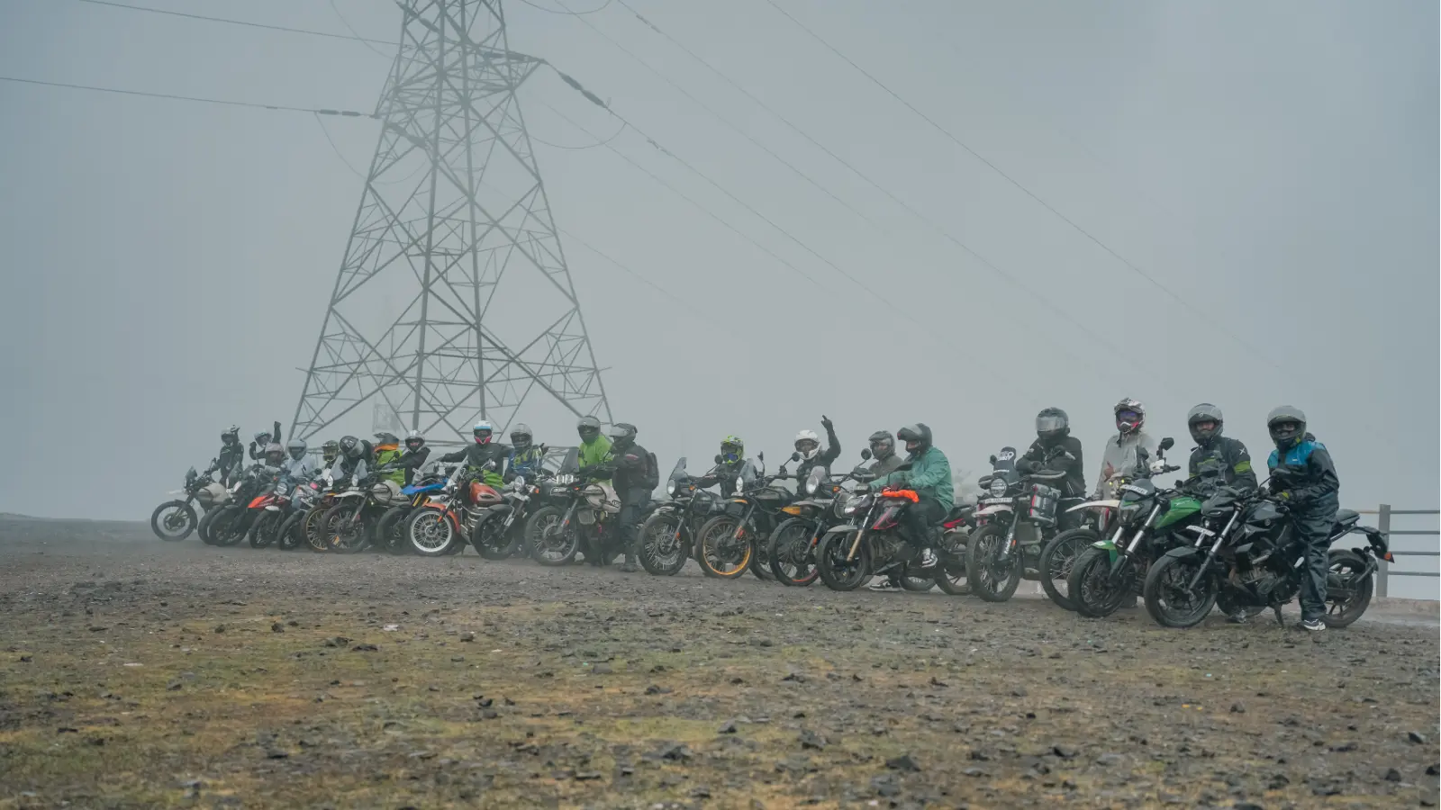 A large group of adventure riders and motorcycles gathered at a misty hilltop viewpoint during a monsoon ride.