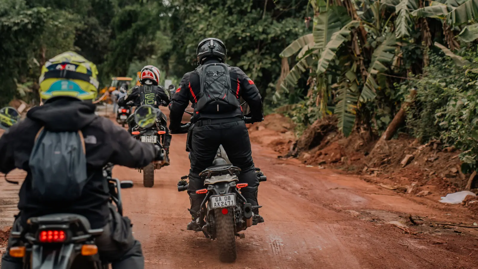 Adventure riders negotiating a rough muddy forest road with one rider standing on the foot pegs for better balance and control.