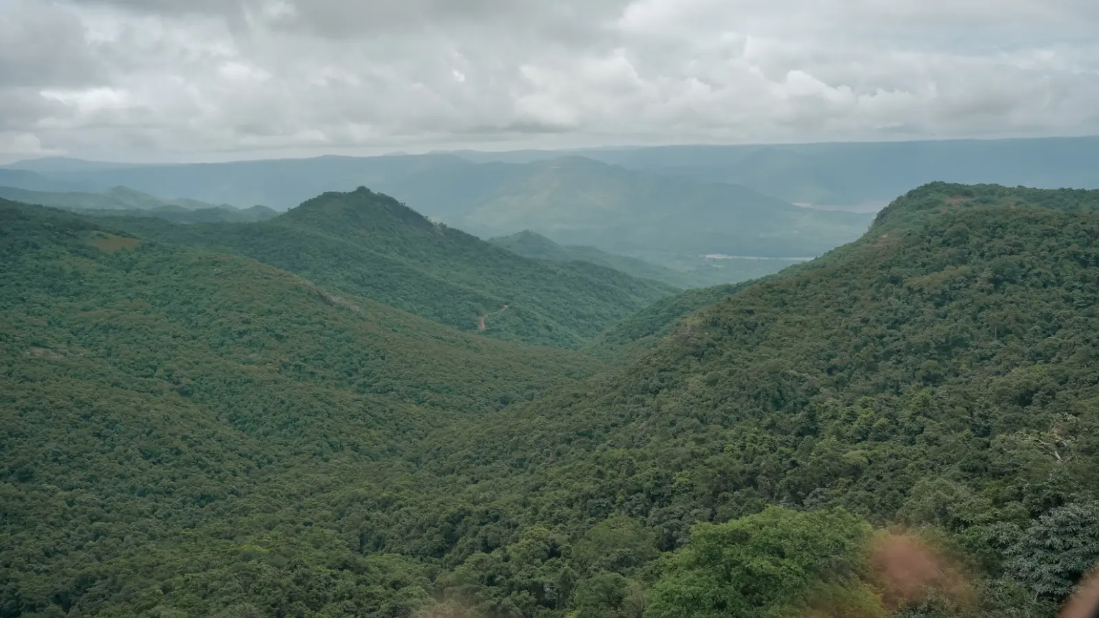 A sweeping view across the forested valleys and rolling hills of the Western Ghats beneath dramatic monsoon skies.
