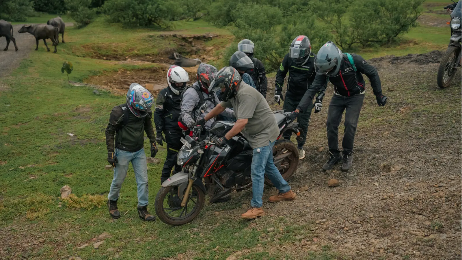A group of adventure riders helps guide a motorcycle down a steep rocky slope during an off road section of the ride.
