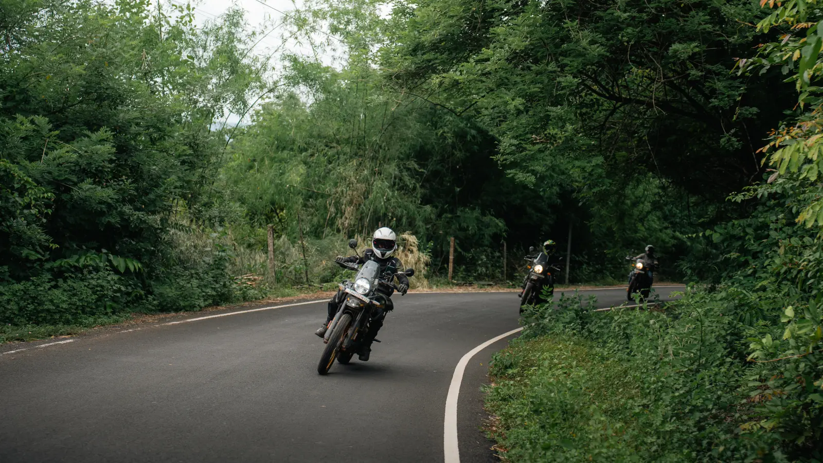 Adventure riders lean through a sweeping forest corner on a winding mountain road as confidence returns with every kilometre.